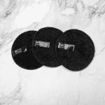 Three black circular reusable makeup remover pads, labeled as "Reusable Makeup Remover Pads - Black," rest elegantly on a white marbled surface.