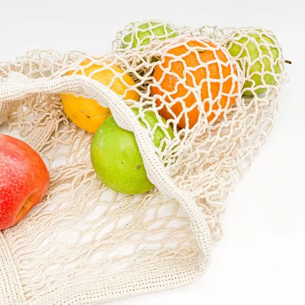 A mesh bag containing a variety of fruits including an apple, a green apple, an orange, a lemon, and a green pear against a white background.